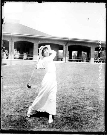 Golfer Ernestine Pearce following through after swinging a golf club on the lawn of an unidentified golf course - Chicago Daily News, Inc.
