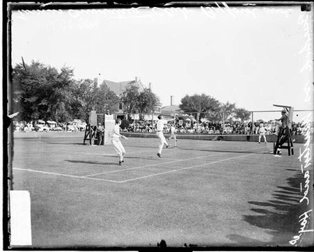 Tennis player following through after hitting a shot in a doubles match on a tennis court at the Onwentsia Club - Chicago Daily News, Inc.