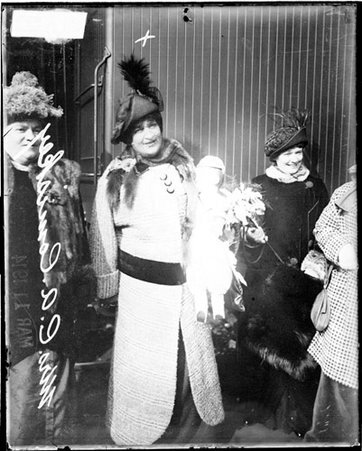 Mrs Charles A Comiskey, wife of Charles A Comiskey, owner White Sox, holding a doll, standing in a railroad station - Chicago Daily News, Inc.