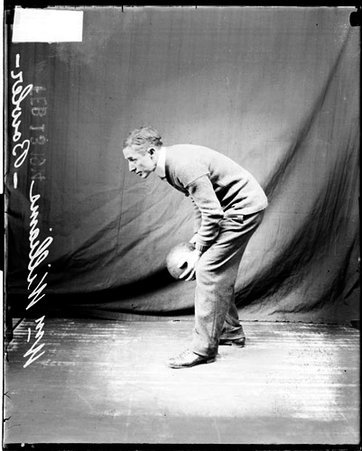Bowler, Williams holding a bowling ball with both hands and leaning forward, standing in front of a dark backdrop in a room - Chicago Daily News, Inc.
