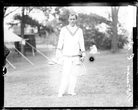 Australian tennis player Norman E Brookes holding two tennis rackets, standing on a grass area - Chicago Daily News, Inc.