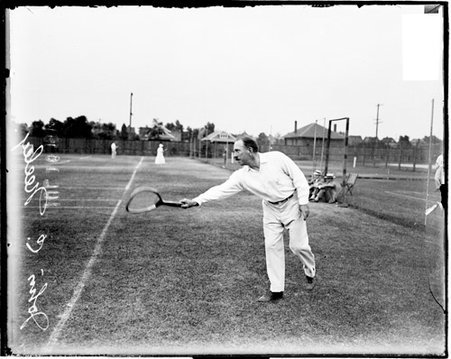Tennis player John C Neely holding a tennis racket out in front of him, standing behind the baseline on a tennis court - Chicago Daily News, Inc.