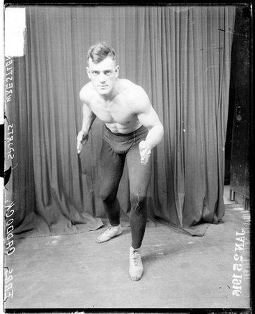Wrestler, Earl Caddock, standing in wrestling stance in front of a dark backdrop - Chicago Daily News, Inc.