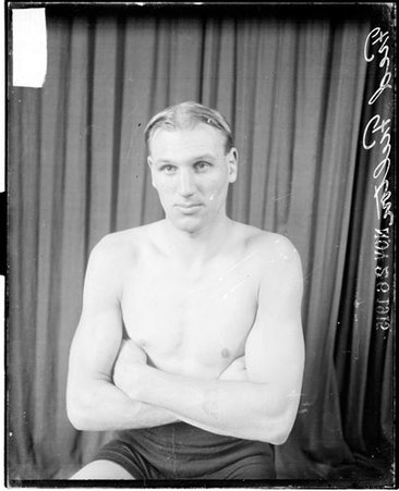 Pugilist, Fred Fulton, with arms crossed, sitting in front of a dark backdrop - Chicago Daily News, Inc.