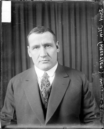 Wrestler, John Olin sitting in front of dark backdrop wearing dark suit and patterned tie - Chicago Daily News, Inc.