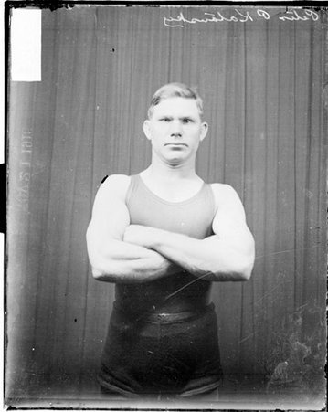 Wrestler, Peter P. Katausky standing with arms crossed in front of dark backdrop - Chicago Daily News, Inc.