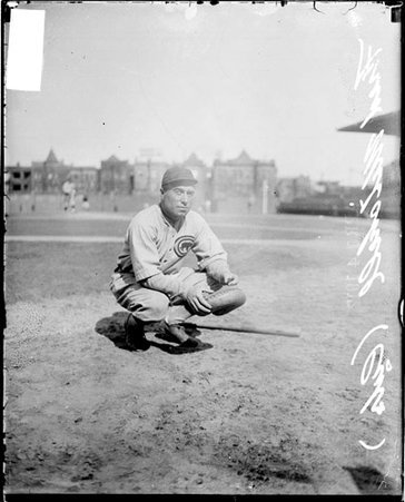 Baseball player, Fred Mitchell squatting on field at Weeghman Park with buildings visible in background, Cubs - Chicago Daily News, Inc.