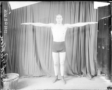 Pugilist, Fred Fulton, with arms extended out to his sides, standing in front of dark backdrop - Chicago Daily News, Inc.