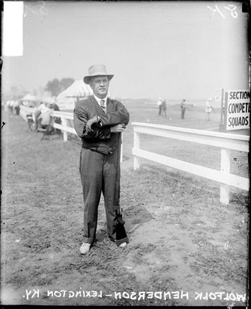 Shooter, Woolfolk Henderson resting arms on rifle standing next to light fence with other shooters in background - Chicago Daily News, Inc.