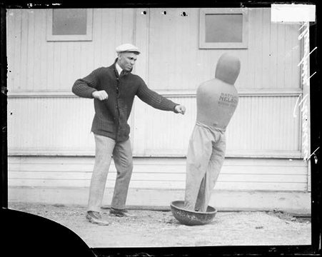 Boxer, Jack Dempsey drawing back his right arm while facing a punching dummy meant to represent pugilist 