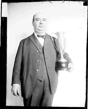 Checkers player Pete Kelley holding a trophy, standing in front of a light-colored backdrop in a room - Chicago Daily News, Inc.