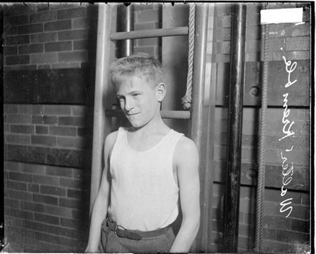 Mozart Playground wrestler Walter Kremble standing in front of a brick wall and a ladder in a room - Chicago Daily News, Inc.