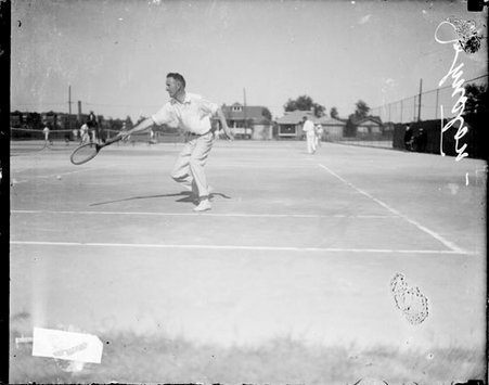 Tennis player, Johnston holding a tennis racket in front of him, standing in profile on a tennis court - Chicago Daily News, Inc.
