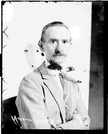 Hans Hansen wearing a suit, sitting in front of a backdrop in a room - Chicago Daily News, Inc.