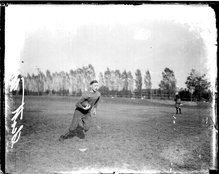 Northwestern University football player Scott holding a football and running on an athletic field - Chicago Daily News, Inc.