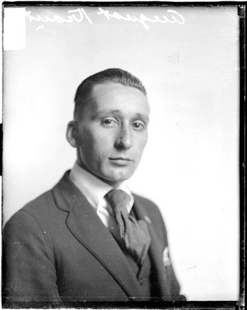 August Kraut wearing a suit, sitting in front of a backdrop in a room - Chicago Daily News, Inc.