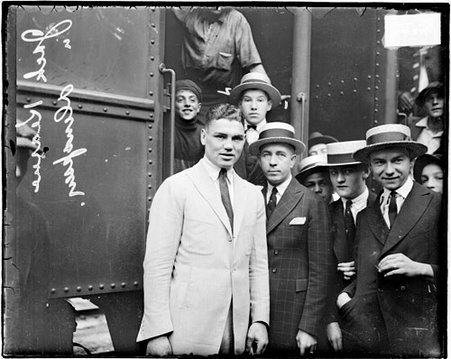 Boxer, Jack Dempsey, standing with manager Jack Kearns in front of a passenger train car in a railroad station - Chicago Daily News, Inc.