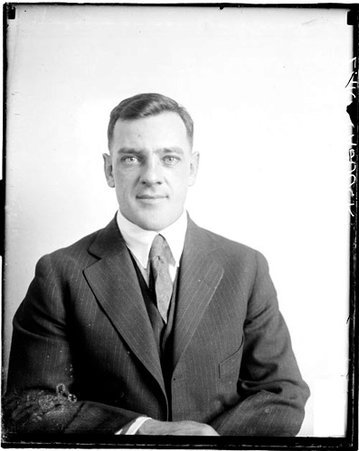 Wrestler Earl Caddock wearing street clothes, sitting in front of a light-colored backdrop in a room - Chicago Daily News, Inc.