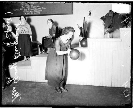 Bowler, Mrs. George Brignall holding a bowling ball and leaning forward, standing in front of a tiered structure in a room - Chicago Daily News, Inc.