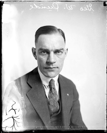 George W. Sunde wearing a checkered suit, sitting in front of a light-colored backdrop in a room - Chicago Daily News, Inc.