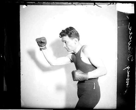 Pugilist, Jimmy Travers standing in profile in a boxing stance in front of a light-colored backdrop in a room - Chicago Daily News, Inc.