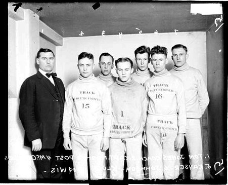 Wisconsin coach Jones, captain Nash, and athletes Post, McCrandless, Kayser, Johnson, and Klug standing in a room - Chicago Daily News, Inc.