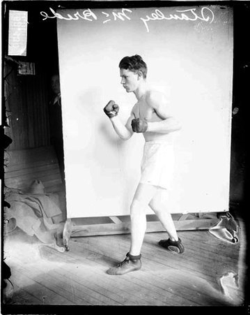 Pugilist, Stanley McBride standing in profile in a boxing stance in front of a light-colored backdrop in a room - Chicago Daily News, Inc.