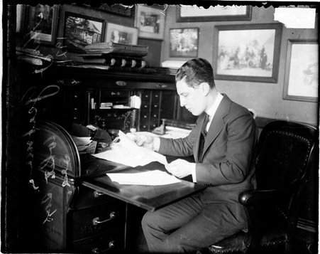 Harry Grabiner, White Sox, looking at a piece of paper that he is holding at a desk in a room - Chicago Daily News, Inc.