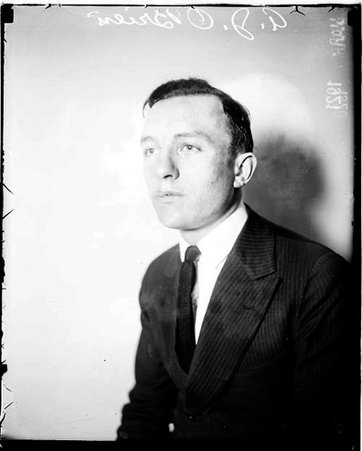 A. J. O'Brien wearing a suit, sitting in front of a light-colored backdrop in a room - Chicago Daily News, Inc.
