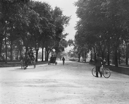 View of Garfield Park - horse-drawn carriage at the left, car with men and bicyclist in the center, man with bike at the left - Unknown