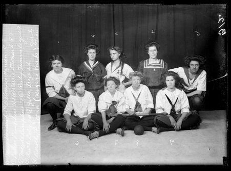 Rogers Park indoor girls' baseball team members sitting and kneeling in front of a dark backdrop - Chicago Daily News, Inc.