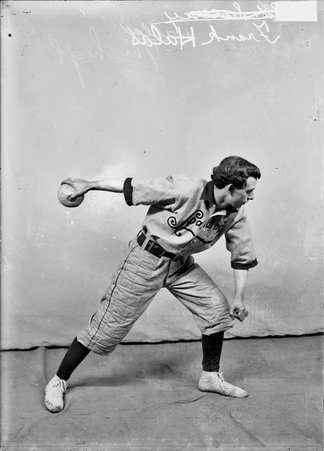 Indoor baseball player, Spalding, Frank Halas, winding up for a pitch in front of a light colored backdrop in a room - Chicago Daily News, Inc.