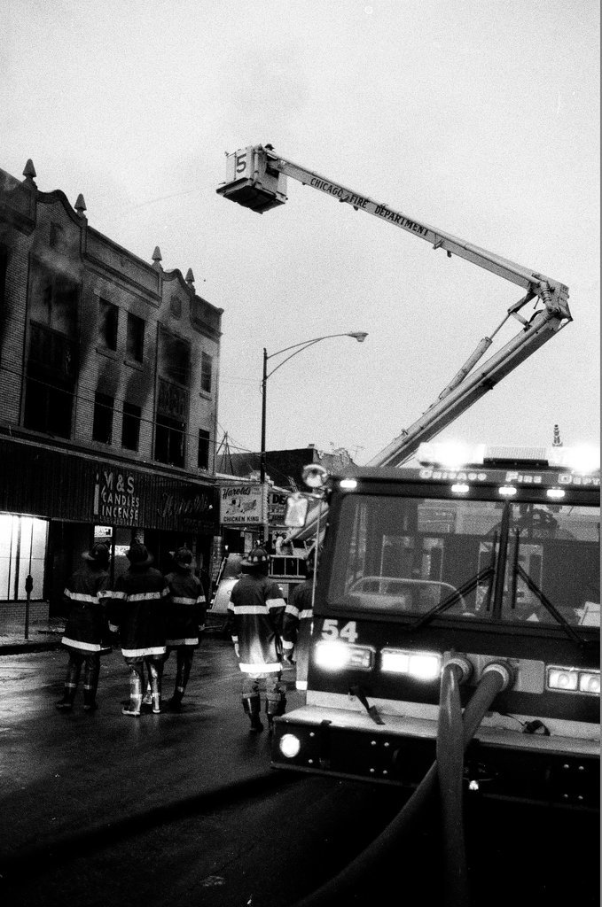 An injured fireman is loaded into an ambulance while remaining firefighters tackle a fire - Chicago Sun-Times