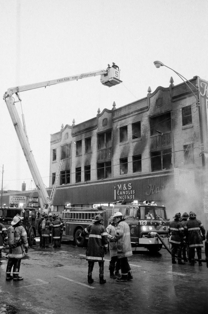 An injured fireman is loaded into an ambulance while remaining firefighters tackle a fire - Chicago Sun-Times