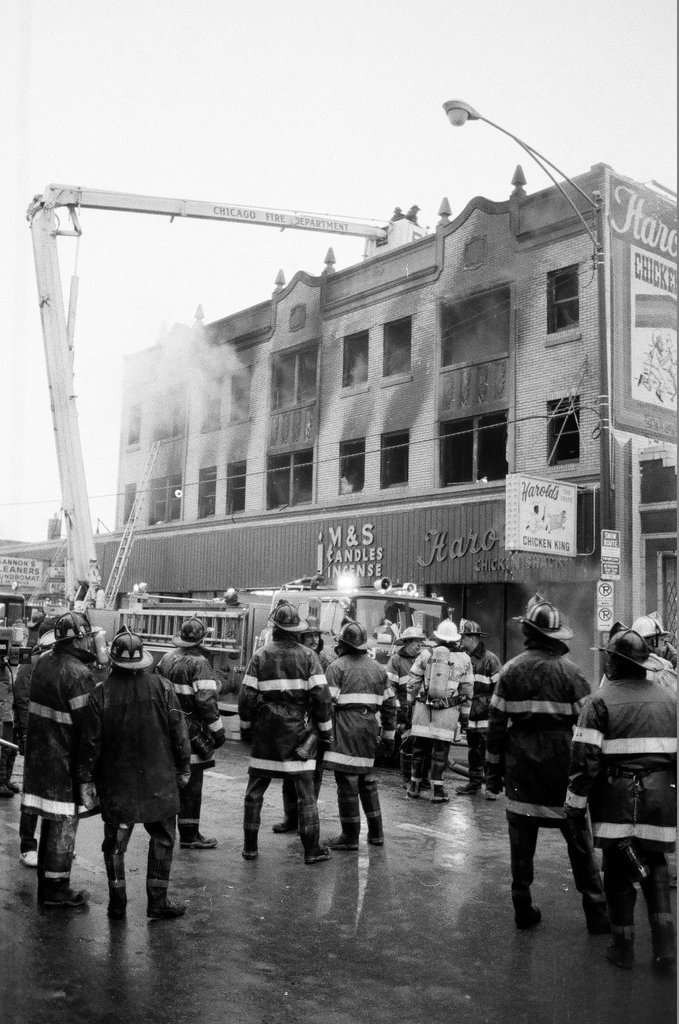 An injured fireman is loaded into an ambulance while remaining firefighters tackle a fire - Chicago Sun-Times