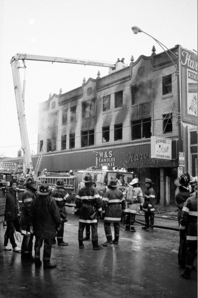An injured fireman is loaded into an ambulance while remaining firefighters tackle a fire - Chicago Sun-Times