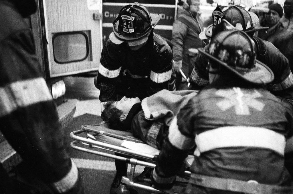 An injured fireman is loaded into an ambulance while remaining firefighters tackle a fire - Chicago Sun-Times